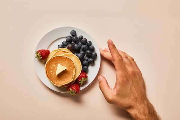 Abgeschnittene Ansicht des Menschen, der Teller mit Pfannkuchen und Beeren auf rosa berührt — Stockfoto