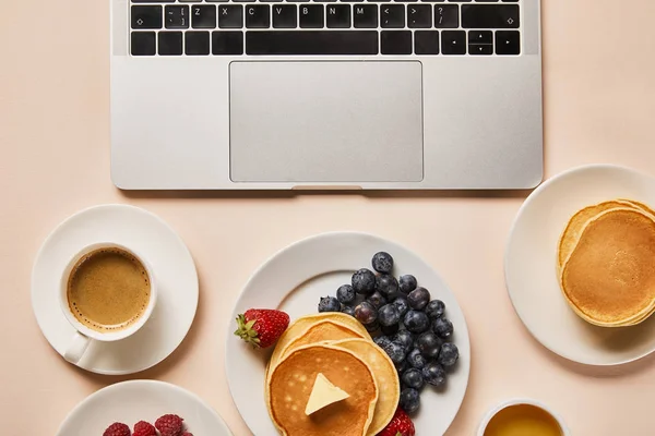 Vista superior do café da manhã saboroso com panquecas, bagas, xícara de café e mel perto do laptop — Stock Photo