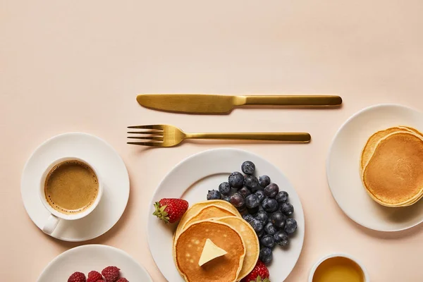 Blick von oben auf leckeres Frühstück mit Pfannkuchen, Beeren, Honig und Kaffee in der Nähe von goldenem Besteck — Stockfoto