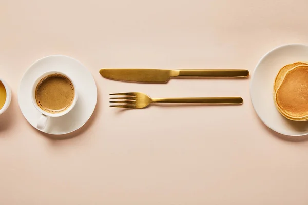 Vista superior da xícara de café com espuma perto de garfo dourado e faca no rosa — Fotografia de Stock