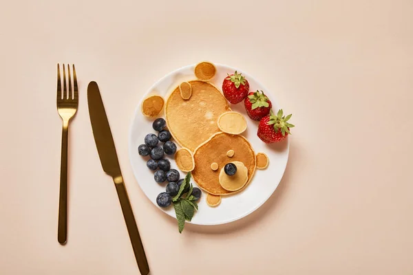 Top view of pancakes, blueberries and strawberries on plate near golden cutlery, bear concept — Stock Photo