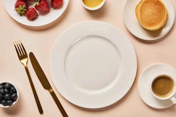 Vista superior del desayuno servido con bayas, café, panqueques y plato vacío en el centro sobre fondo rosa - foto de stock