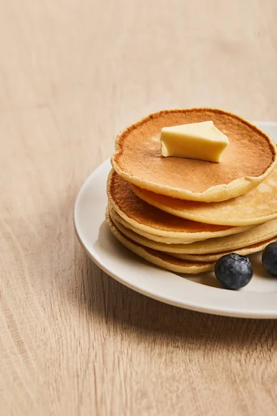 Pancakes with butter and blueberries on plate on wooden surface — Stock Photo
