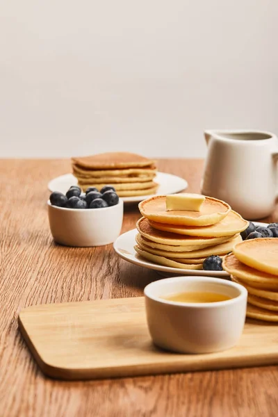 Selektiver Fokus der Teller mit Pfannkuchen, Beeren, Honig in der Schüssel und Sirup in der Kanne isoliert auf grau — Stockfoto