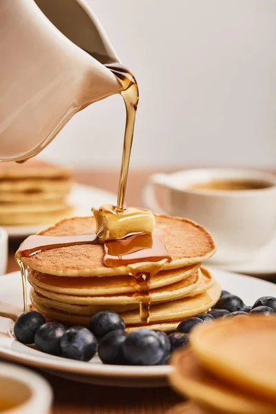 Selektiver Fokus von Sirup auf Pfannkuchen mit Butter und Blaubeeren in der Nähe einer Tasse Kaffee — Stockfoto