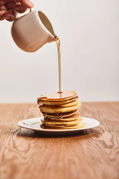 Cropped view of man pouring pancakes on plate on wooden surface isolated on grey — Stock Photo