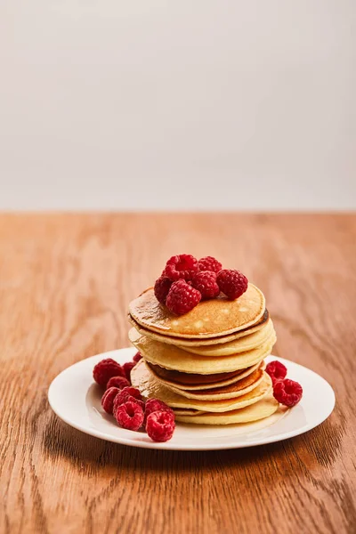 Selective focus of pancakes with raspberries on plate on wooden surface isolated on grey — Stock Photo
