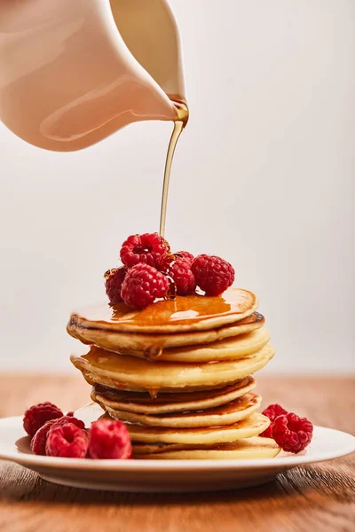 Syrup pouring on pancakes with raspberries on plate on wooden surface isolated on grey — Stock Photo