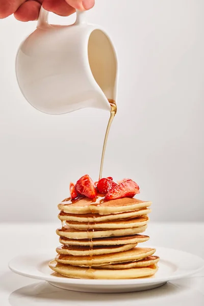 Cropped view of man pouring pancakes with strawberries on plate isolated on grey — Stock Photo