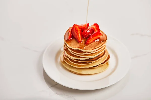 Pouring syrup on tasty pancakes with strawberries on white plate on textured surface — Stock Photo