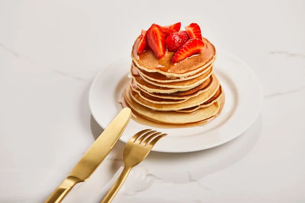 Golden fork and knife on plate with pancakes and strawberries — Stock Photo