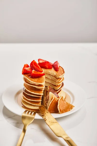 Pancakes with strawberries and fork with knife on plate on textured surface — Stock Photo