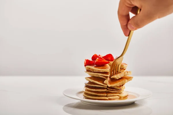 Vue recadrée de l'homme prenant des tranches de crêpes avec fourchette dorée sur plaque blanche isolée sur gris — Photo de stock