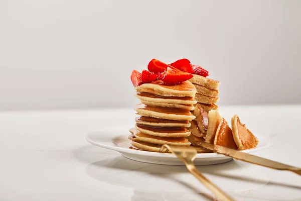 Selective focus of pancakes with strawberries and golden cutlery on white plate isolated on grey — Stock Photo
