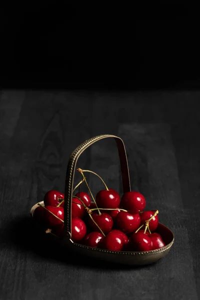 Красные вкусные вишни в металлической корзине на деревянном темном столе изолированы на черном — стоковое фото