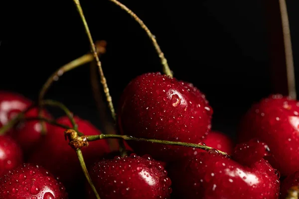 Vue rapprochée de cerises rouges délicieuses avec des gouttes d'eau isolées sur noir — Photo de stock