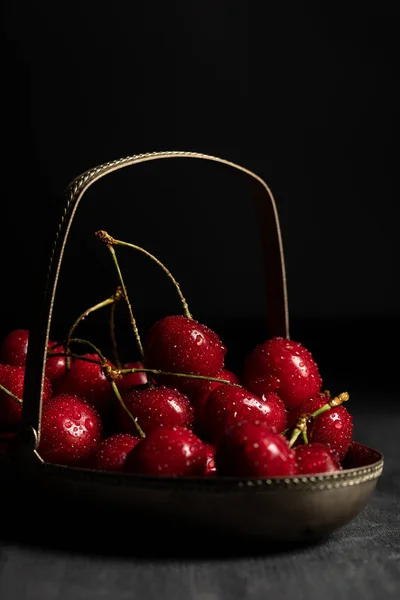 Rojo deliciosas cerezas con gotas de agua en cesta de metal sobre mesa oscura de madera aislado en negro - foto de stock