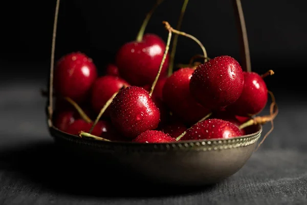 Selective focus of wet red delicious cherries in metal basket on wooden dark table isolated on black — Stock Photo