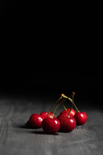 Red tasty cherries with water drops on wooden table isolated on black — Stock Photo