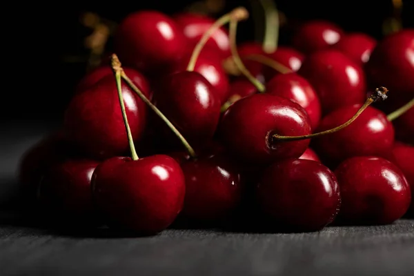 Enfoque selectivo de las deliciosas cerezas rojas dispersas en la mesa oscura de madera - foto de stock