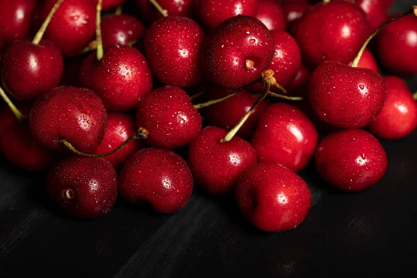 Cerises rouges délicieuses et mûres avec des gouttes d'eau sur tissu noir — Photo de stock