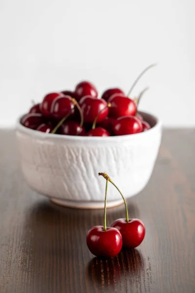 Enfoque selectivo de las cerezas rojas en un tazón blanco sobre una mesa de madera aislada en blanco - foto de stock