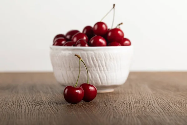 Messa a fuoco selettiva di ciliegie rosse in ciotola su tavolo in legno isolato su bianco — Foto stock