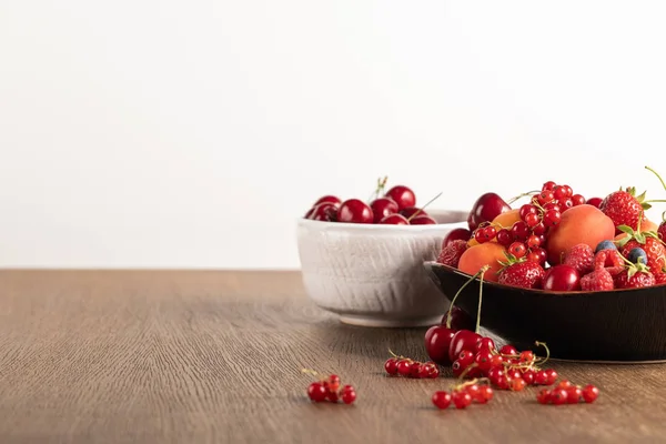 Selective focus of cherries in white bowl and mixed berries on plate on wooden table isolated on white — Stock Photo