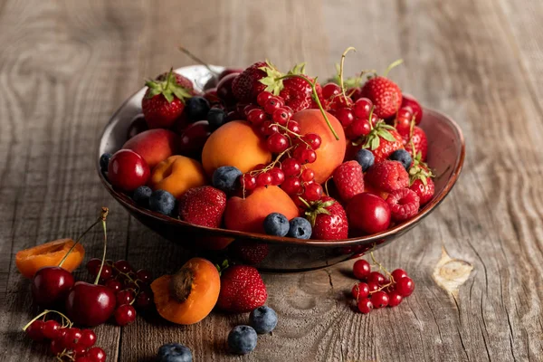 Ripe seasonal berries and apricots on plate on wooden table — Stock Photo