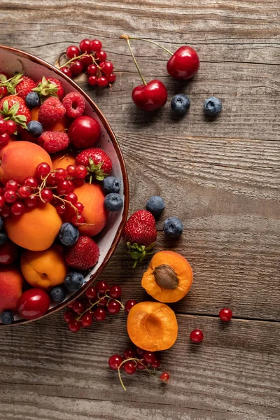 Blick von oben auf reife saisonale Beeren und Aprikosen auf Teller auf Holztisch — Stockfoto