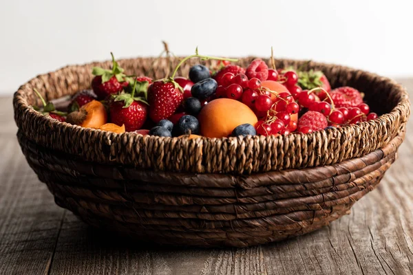 Wicker basket full of seasonal berries on wooden table isolated on white — Stock Photo