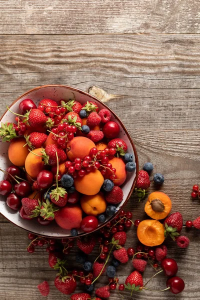 Вид зверху на стиглі свіжі сезонні ягоди та абрикоси на тарілці на дерев'яному столі — стокове фото