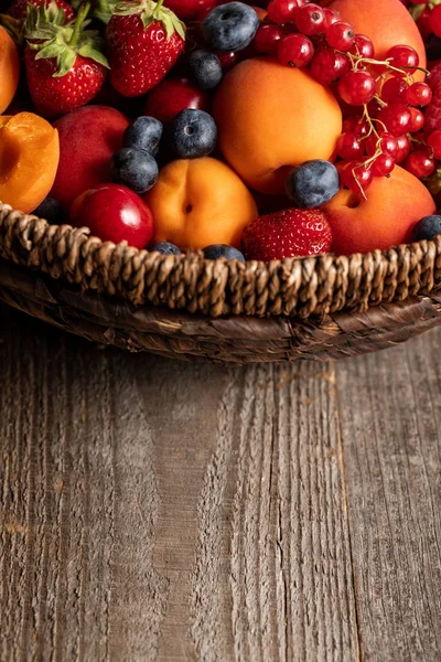 Close up view of ripe seasonal berries and apricots in wicker basket on wooden table — Stock Photo