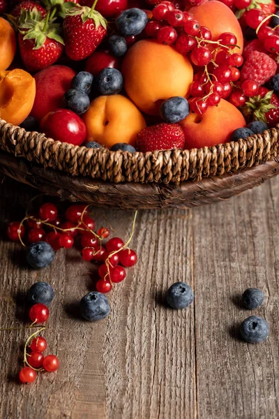 Nahaufnahme von reifen Beeren und Aprikosen in Weidenkorb auf Holztisch — Stockfoto