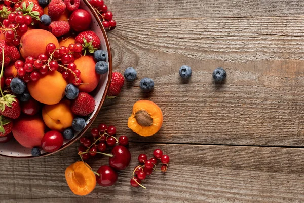 Вид зверху на стиглі свіжі ягоди та абрикоси на тарілці на дерев'яному столі — стокове фото