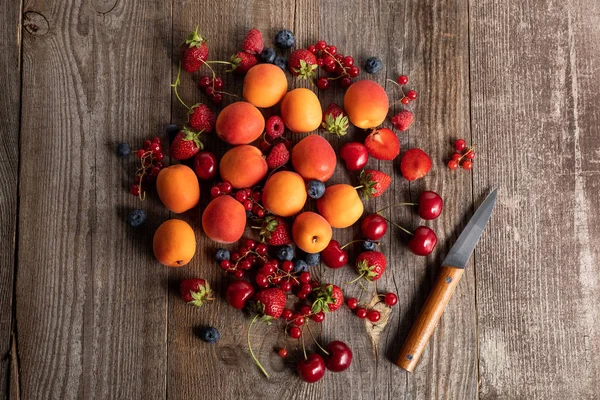 Top view of ripe delicious fresh berries and apricots on wooden table with knife — Stock Photo