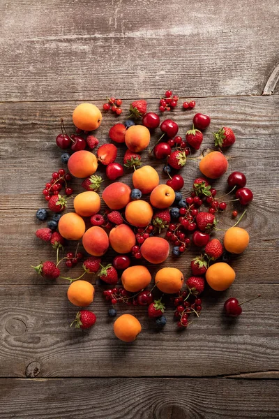 Vue de dessus des baies fraîches mûres délicieuses et des abricots savoureux sur la table en bois — Photo de stock