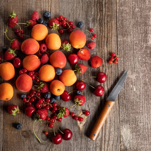 Top view of ripe delicious seasonal berries scattered with fresh apricots on wooden table near knife — Stock Photo