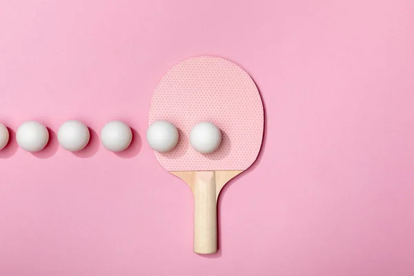 Плоска лежала з білими кульками для пінг-понг та ракеткою на рожевому фоні — стокове фото