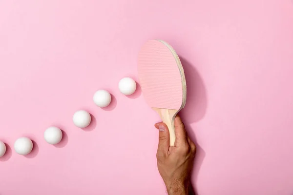 Vista recortada del hombre sosteniendo raqueta de tenis de mesa cerca de bolas blancas sobre fondo rosa - foto de stock