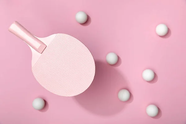 Vista superior de bolas de tenis de mesa blancas dispersas bajo raqueta sobre fondo rosa - foto de stock