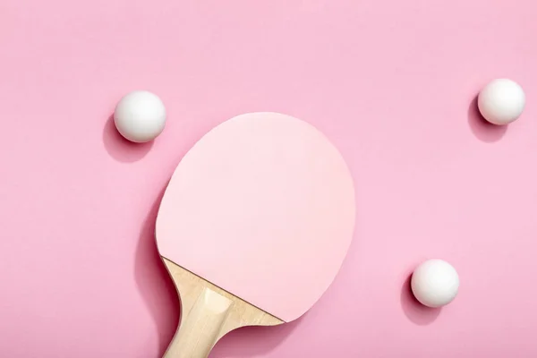 Vista superior de bolas de tenis de mesa blancas dispersas cerca de raqueta rosa sobre fondo rosa - foto de stock