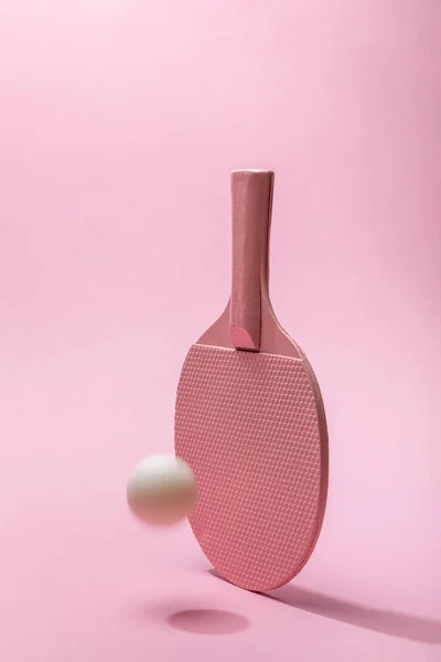 Ракетка для пинг-понга и белый летящий шар на розовом фоне с копировальным пространством — стоковое фото
