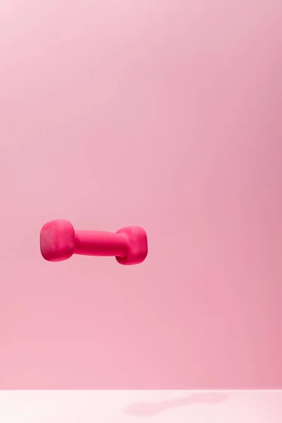 Pink bright dumbbell levitating in air on pink background — Stock Photo