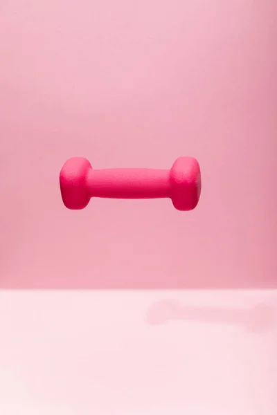 Pink bright dumbbell levitating in air on pink background — Stock Photo
