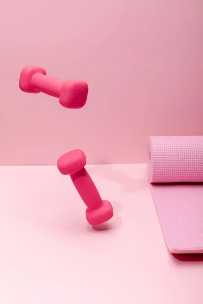 Pink bright dumbbells levitating in air near rubber fitness mat on pink background — Stock Photo