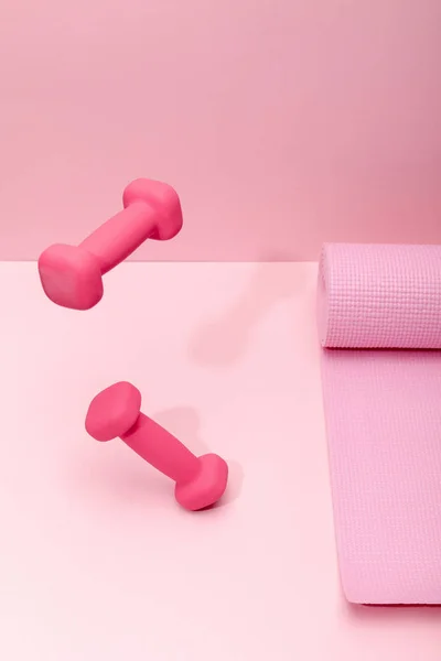 Halteres brilhantes rosa levitando no ar perto de tapete de fitness no fundo rosa — Fotografia de Stock