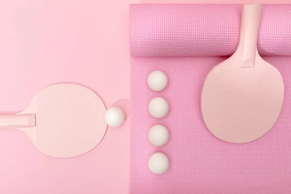 Vista dall'alto di palline da ping-pong bianche e racchette su tappetino fitness su sfondo rosa — Foto stock