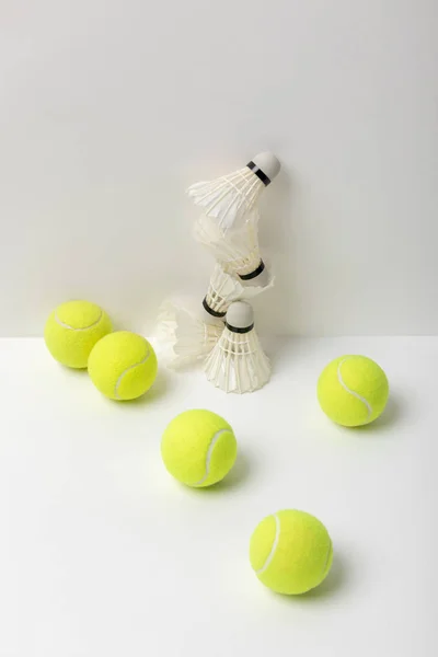 Navette bianche badminton e palle da tennis giallo brillante su sfondo bianco — Foto stock