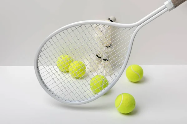 Pollas blancas de bádminton y pelotas de tenis de color amarillo brillante cerca de la raqueta sobre fondo blanco - foto de stock